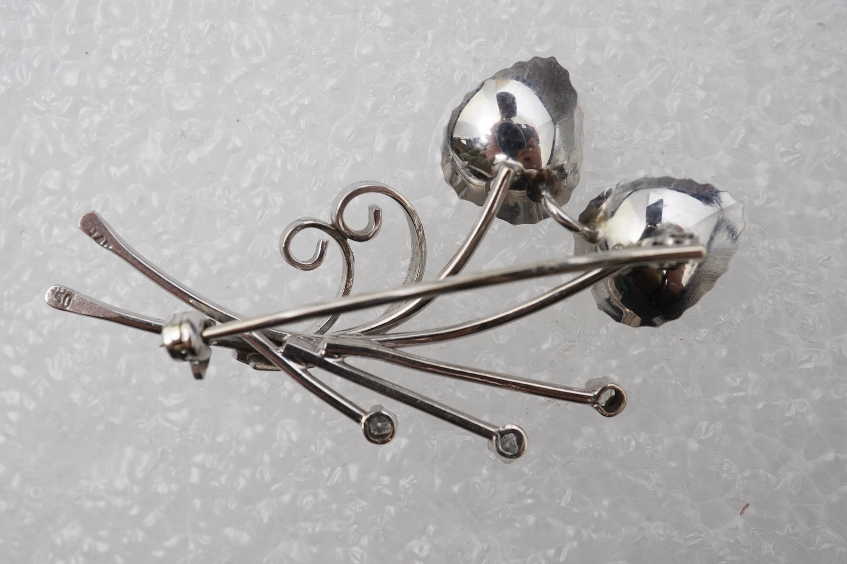 A diamond brooch, designed as stylised foliate spray in white gold, accented with three brilliant-cut diamonds totalling approximately 0.15 carats, length 5.2cm, stamped 750, gross weight 5 grams.